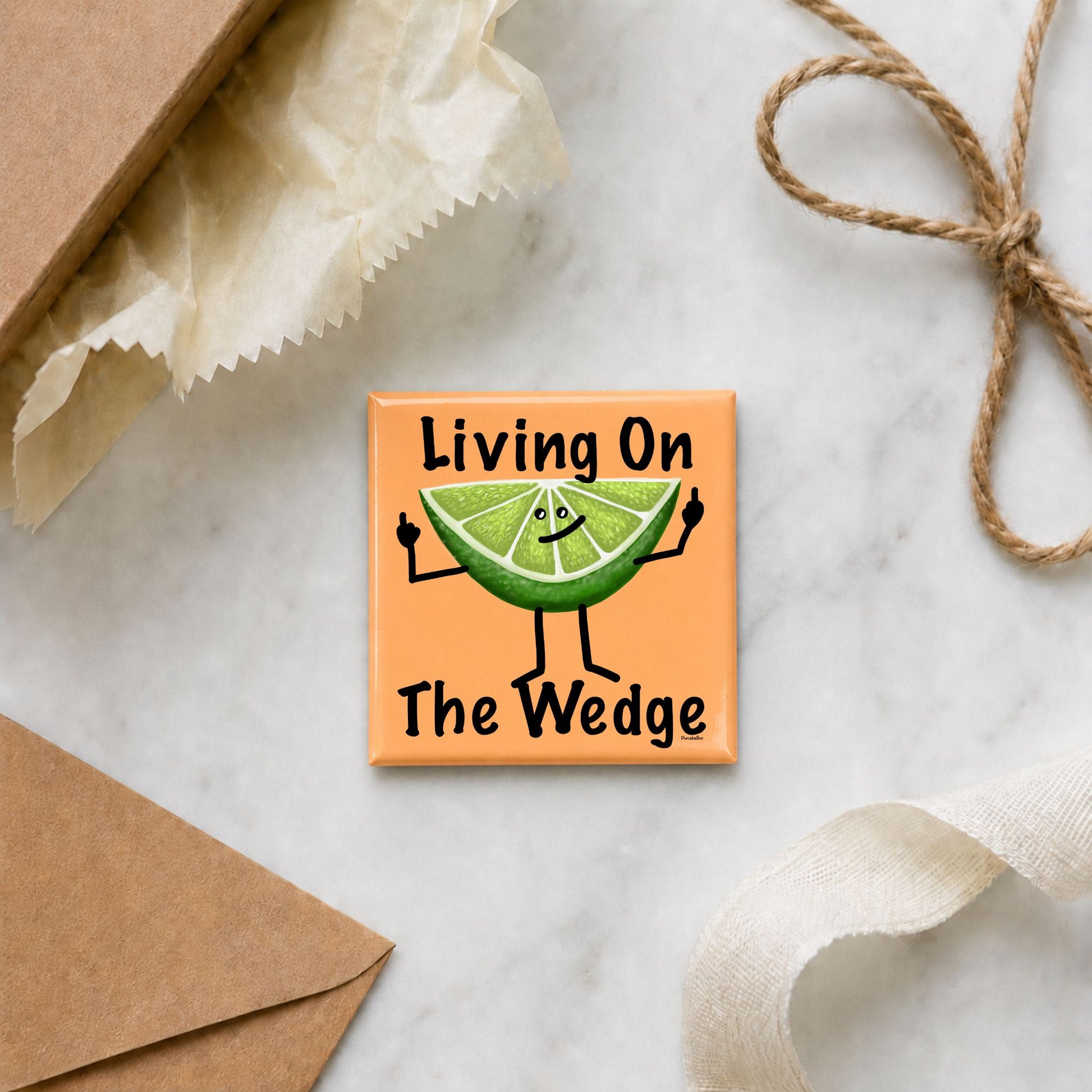 Funny lime magnet arranged with gift wrap, an envelope, ribbon, and twine
