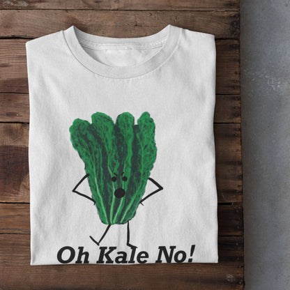 A folded white t-shirt with a green kale character graphic and the text 'Oh Kale No!' is displayed on a rustic wooden surface, with white sneakers partially visible at the bottom.