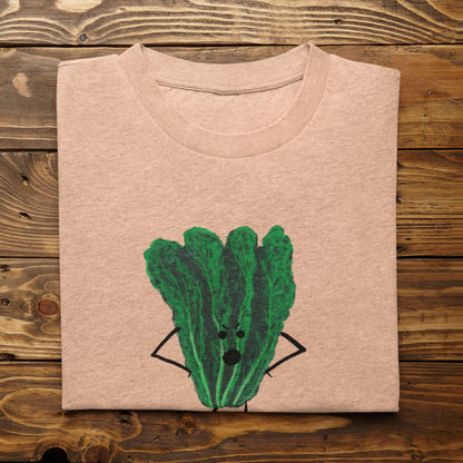 A folded light heather peach t-shirt with Oh Kale No pun printed on the front, displayed flat on a rustic wooden plank background.