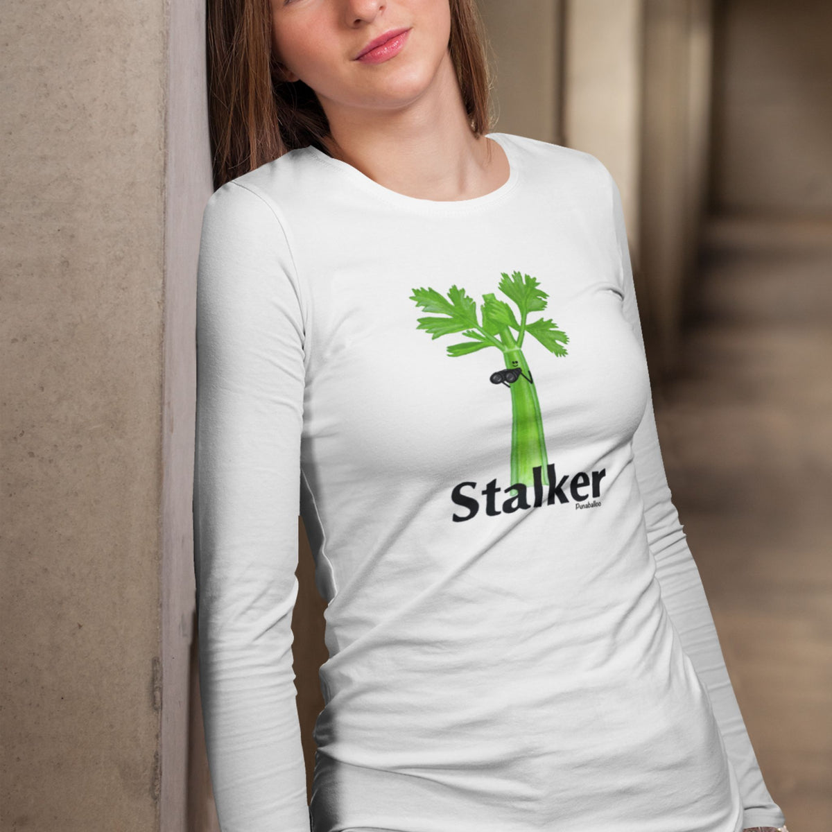 Woman wearing a white Stalker long sleeve shirt with a celery stalk holding binoculars