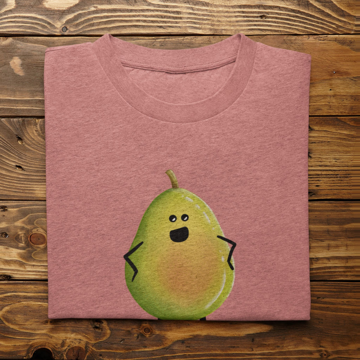 A folded heathered mauve t-shirt featuring a cute cartoon pear character printed on the front, displayed flat on a rustic wooden plank background.