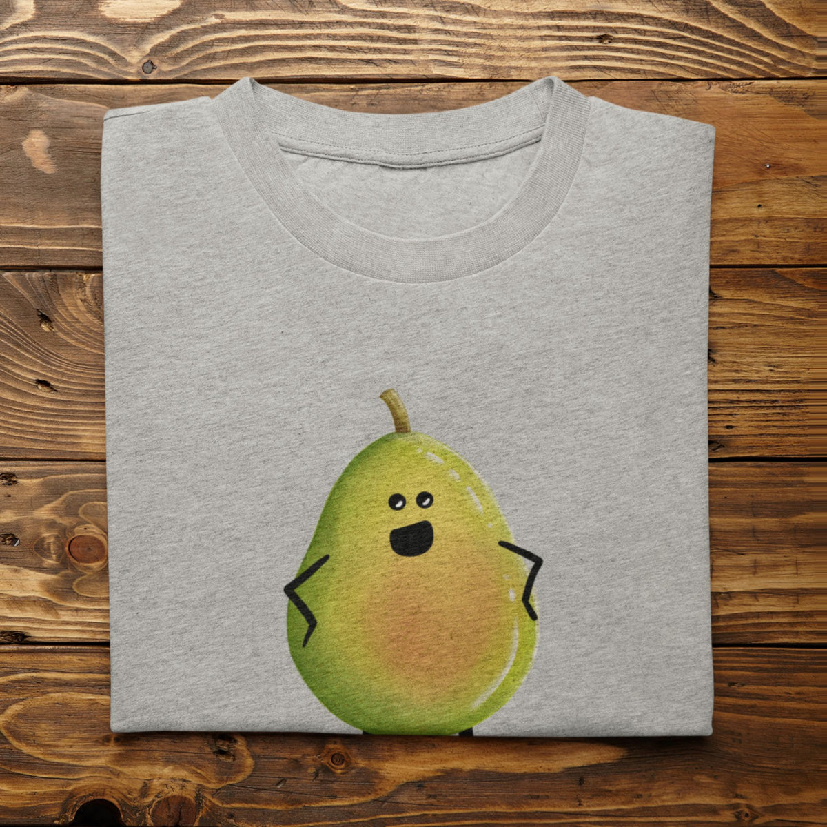 A folded light gray t-shirt with a cute cartoon pear graphic, displayed flat on a rustic wooden plank background.
