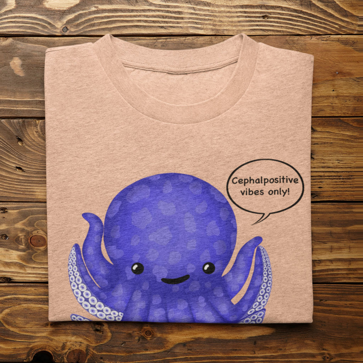 Heather peach T-shirt flat lay featuring the purple Eternal Octomist octopus and Cephalopositive vibes only design.