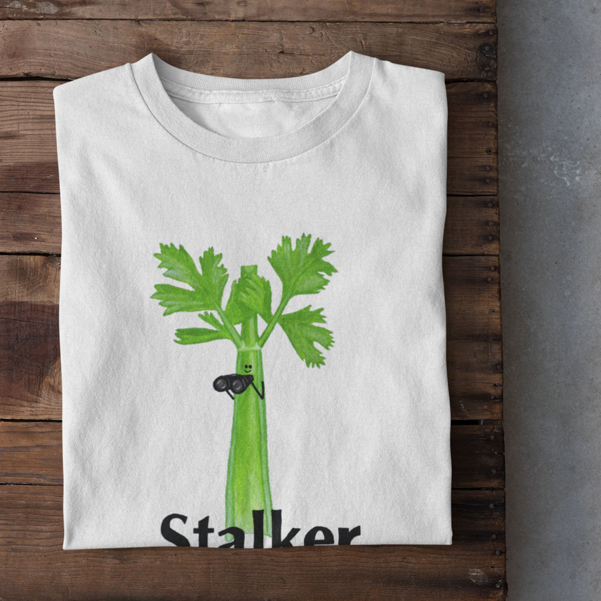 White Stalker celery pun T-shirt flat lay featuring a green celery character holding binoculars.