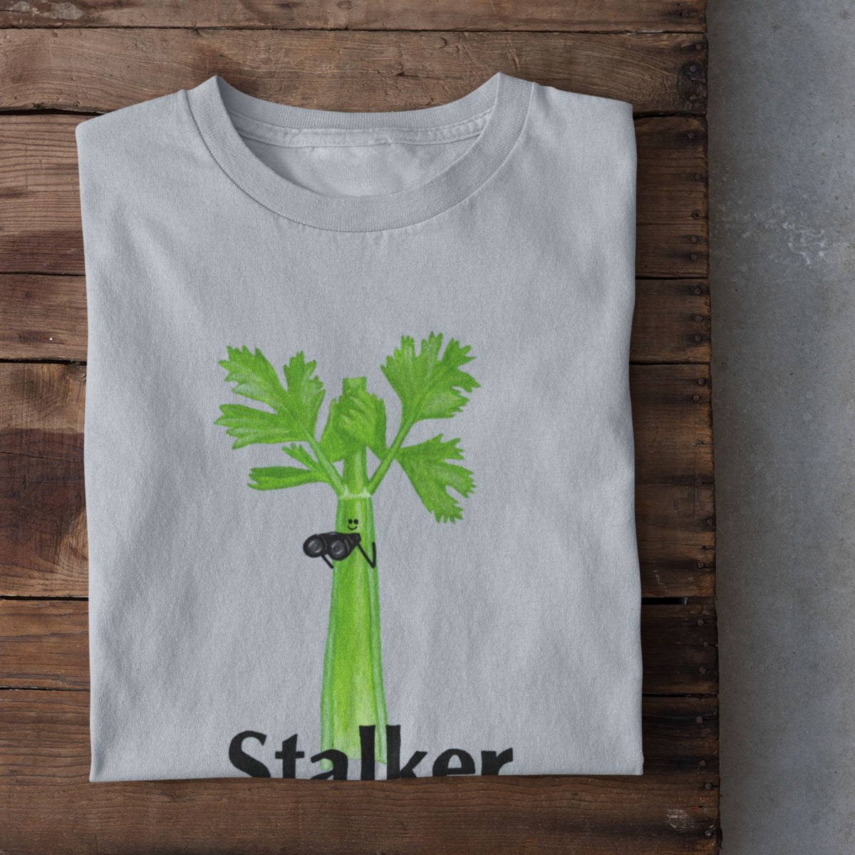 Light blue Stalker celery pun T-shirt flat lay featuring a green celery character holding binoculars.