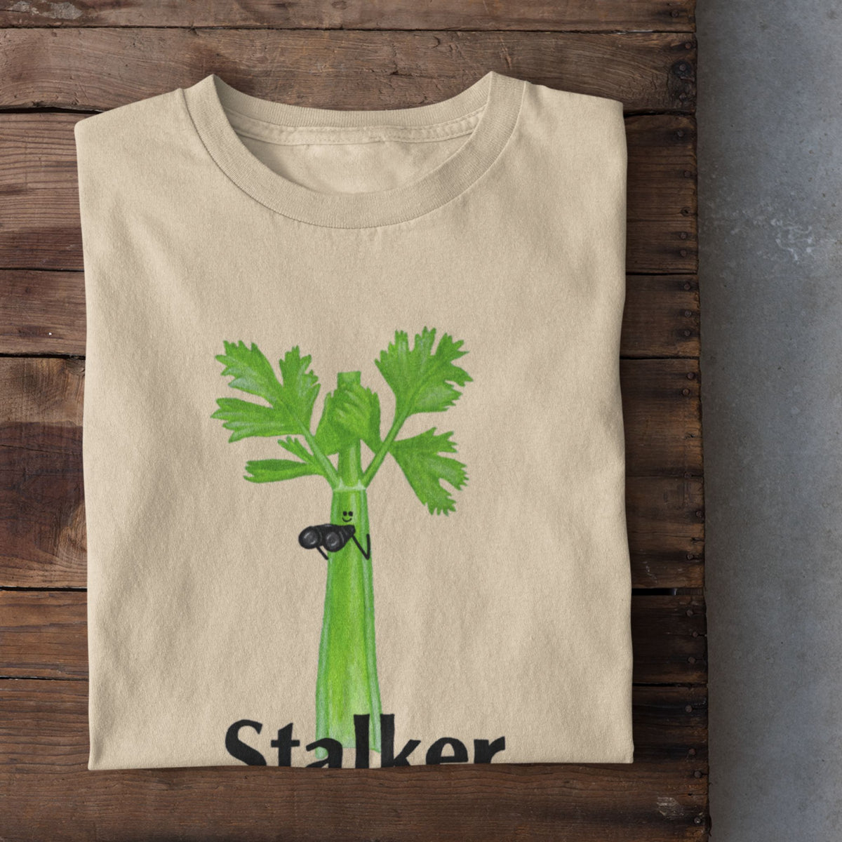 Soft cream Stalker celery pun T-shirt flat lay featuring a green celery character holding binoculars.