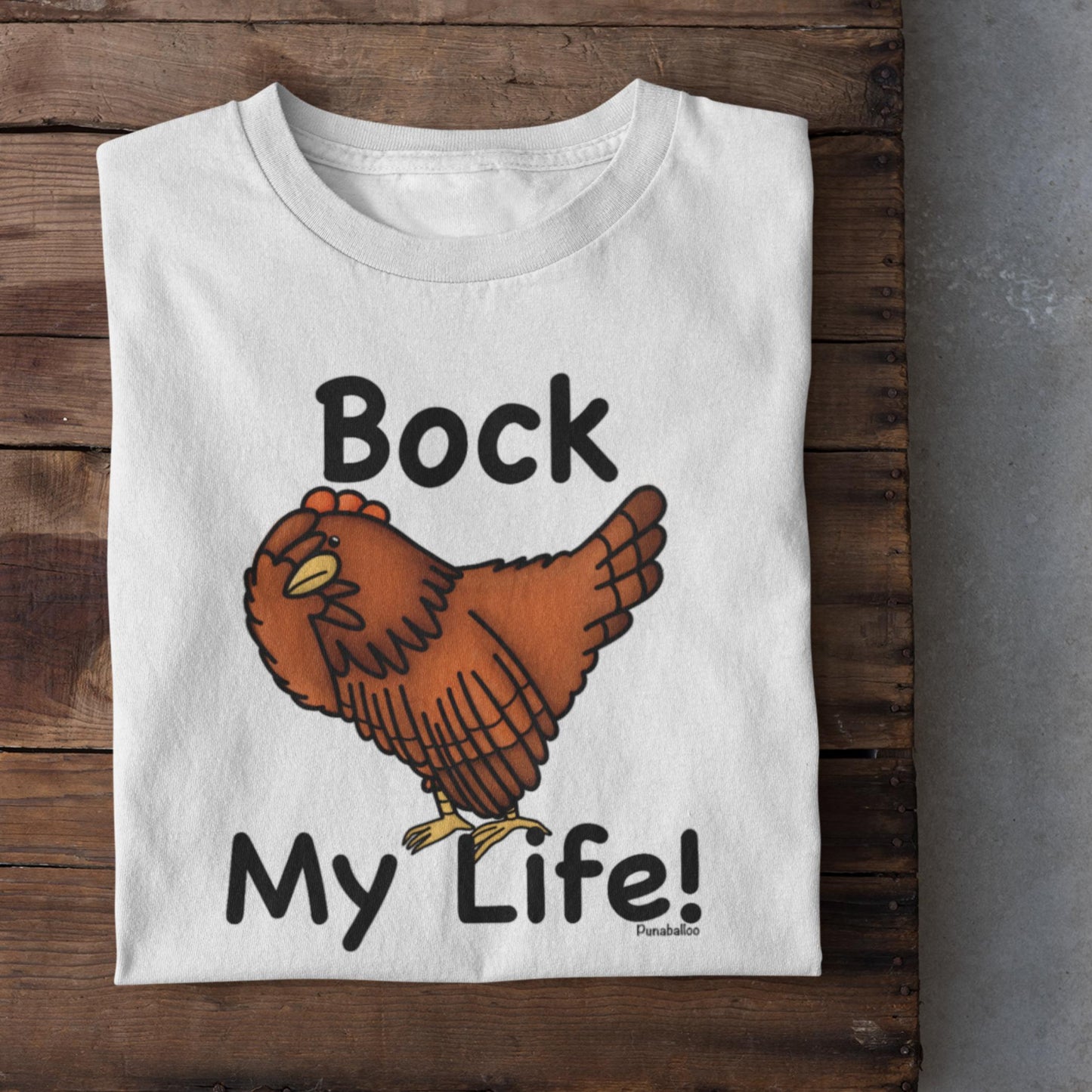 White folded Bock My Life poultry pun t-shirt shown on a rustic wooden surface