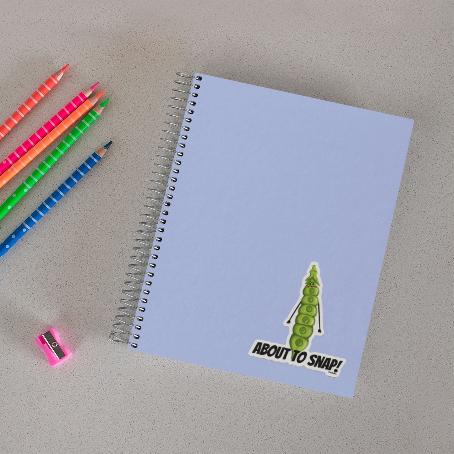 About to Snap vegetable pun sticker on a notebook beside colored pencils
