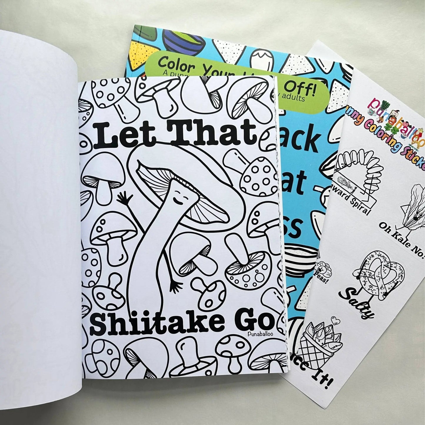 Adult coloring book bundle open to funny food pun page Let That Shiitake Go with sticker sheet included