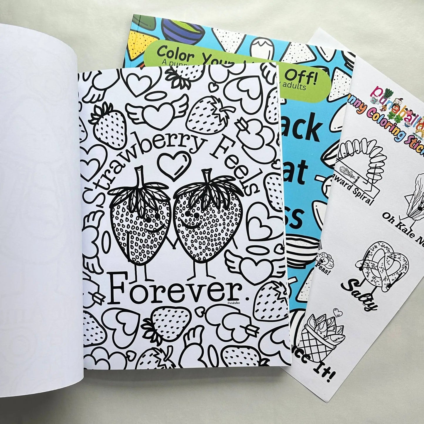 Adult coloring book set open to Strawberry Feels Forever pun page with matching coloring sticker sheet
