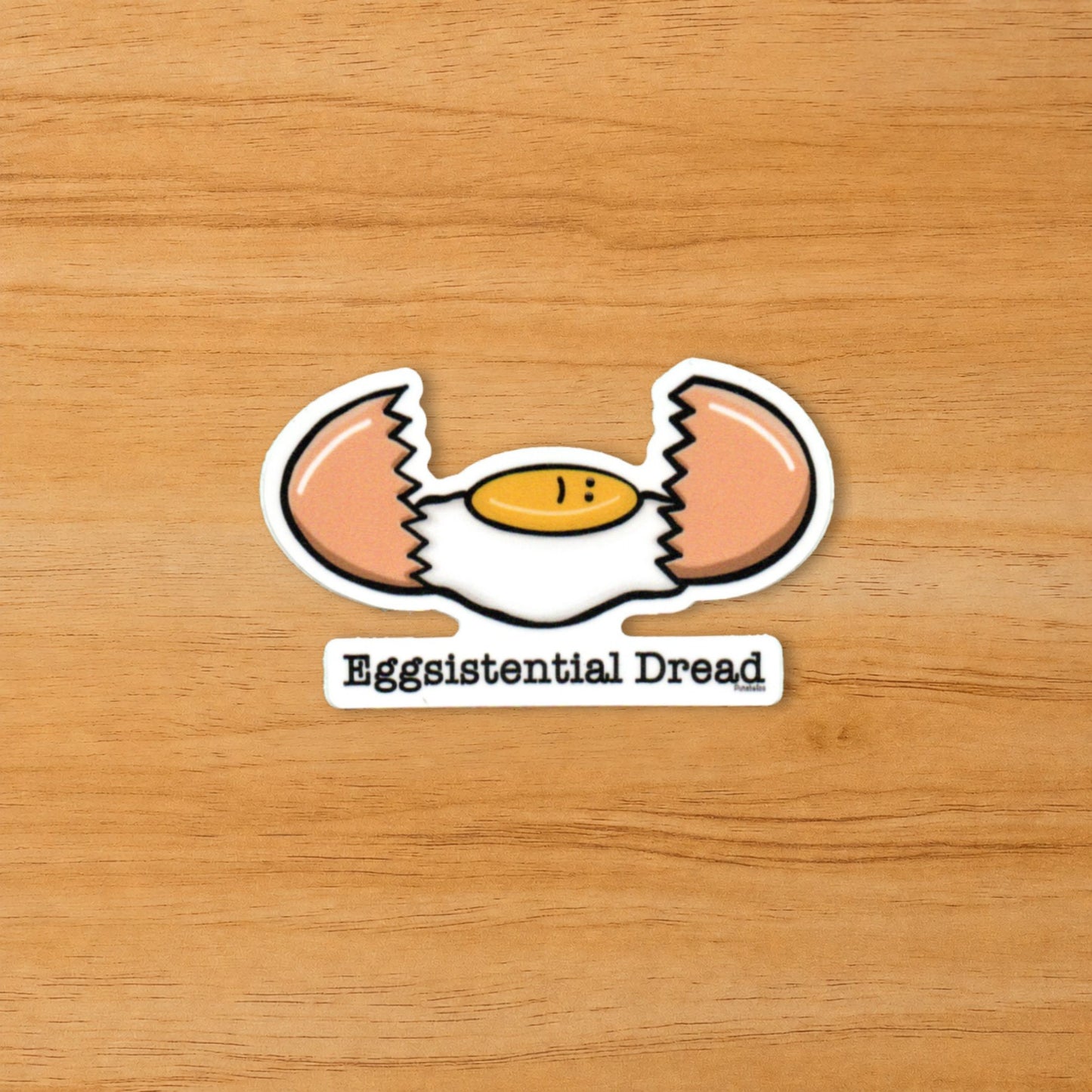 Eggsistential Dread dark humor egg sticker on a wood surface