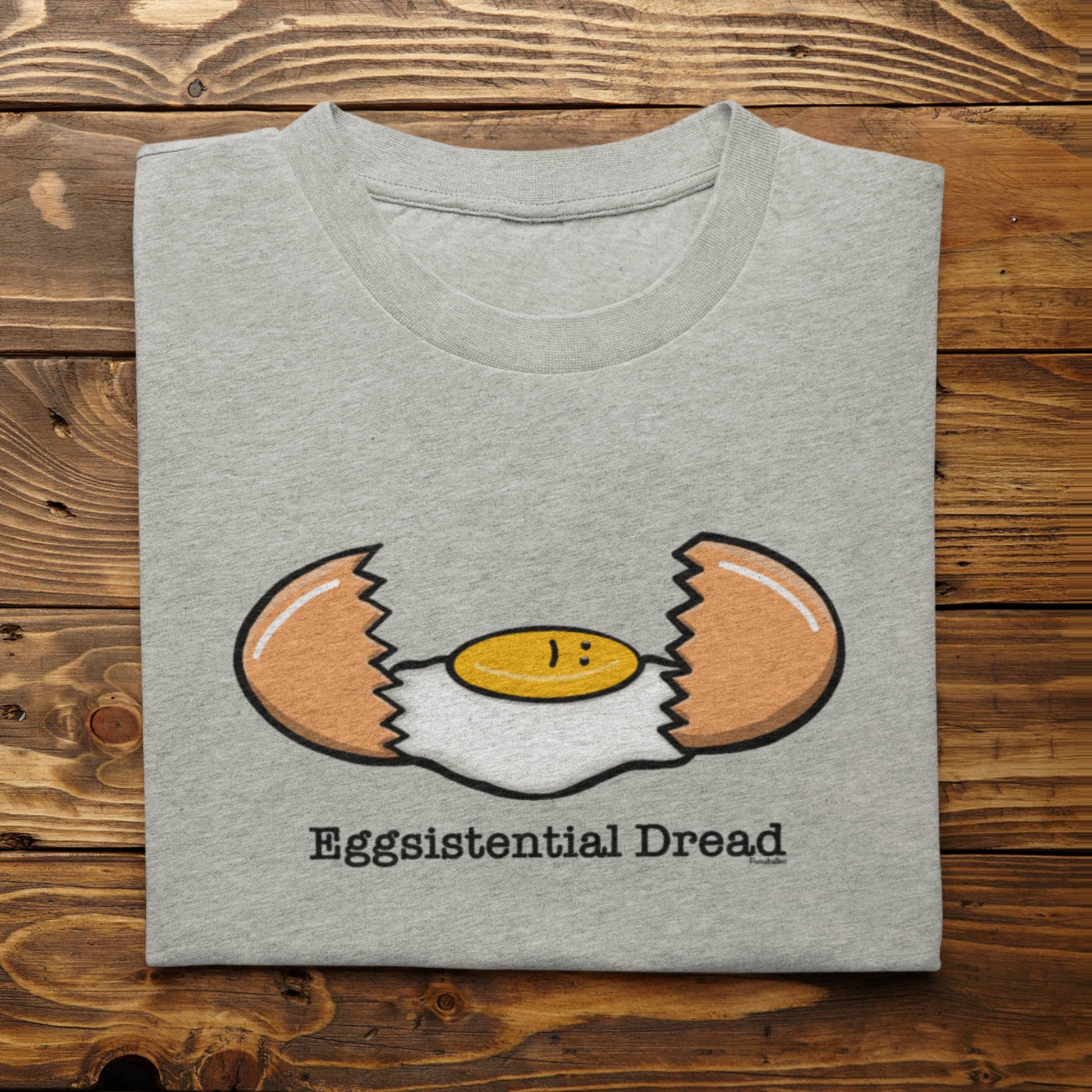 Folded athletic heather Eggsistential Dread dark humor breakfast shirt on rustic wood background
