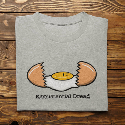 Folded athletic heather Eggsistential Dread dark humor breakfast shirt on rustic wood background