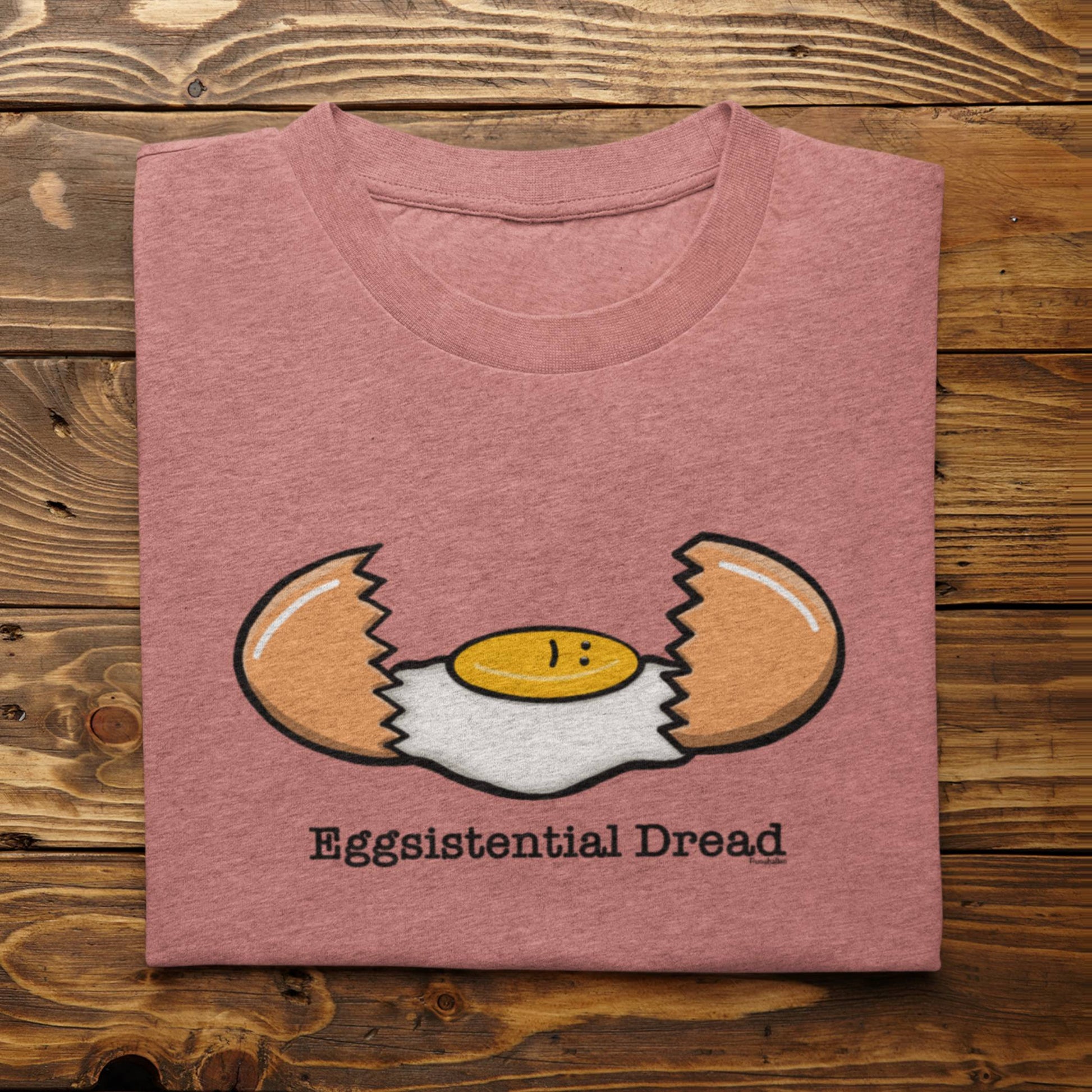 Folded heather mauve Eggsistential Dread egg pun t-shirt on rustic wood background