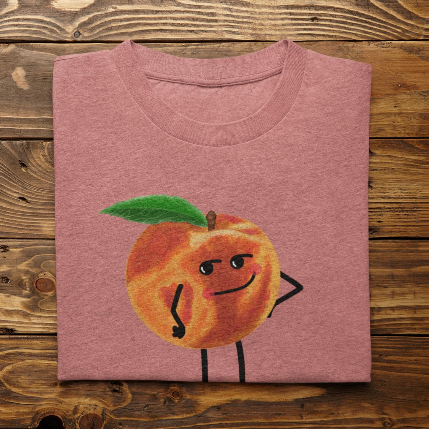 Folded heather mauve Karma Is a Peach peach pun t-shirt on rustic wood background