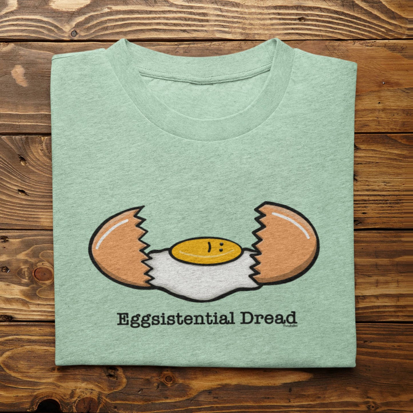 Folded heather mint Eggsistential Dread breakfast pun shirt on rustic wood background