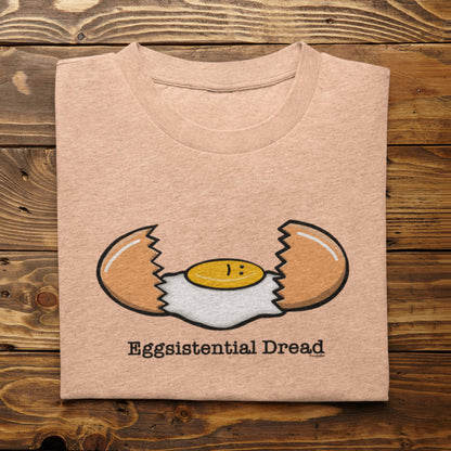 Folded heather peach Eggsistential Dread funny egg t-shirt on rustic wood background