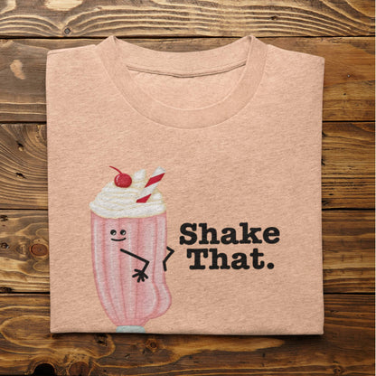 Folded heather peach Shake That milkshake pun t-shirt on rustic wood background