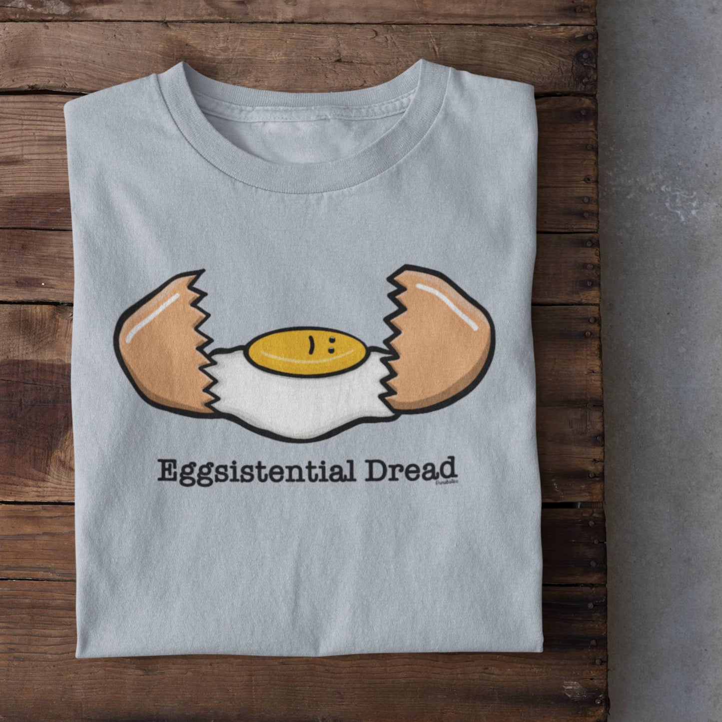 Folded light blue Eggsistential Dread egg t-shirt on rustic wood background
