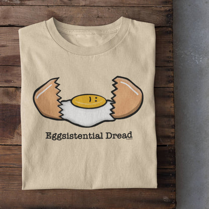Folded soft cream Eggsistential Dread dark humor egg shirt on rustic wood background