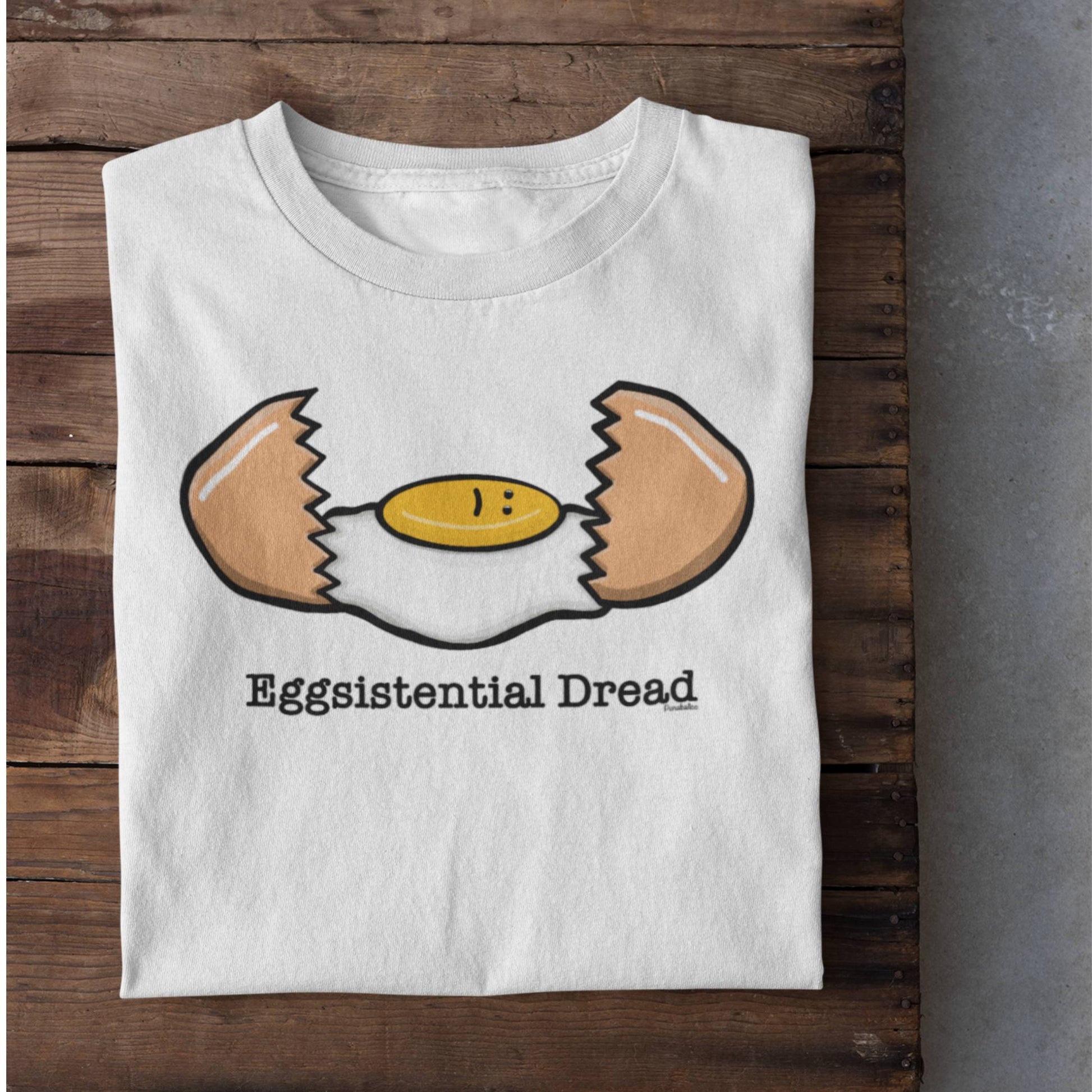 Folded white Eggsistential Dread egg t-shirt on rustic wood background