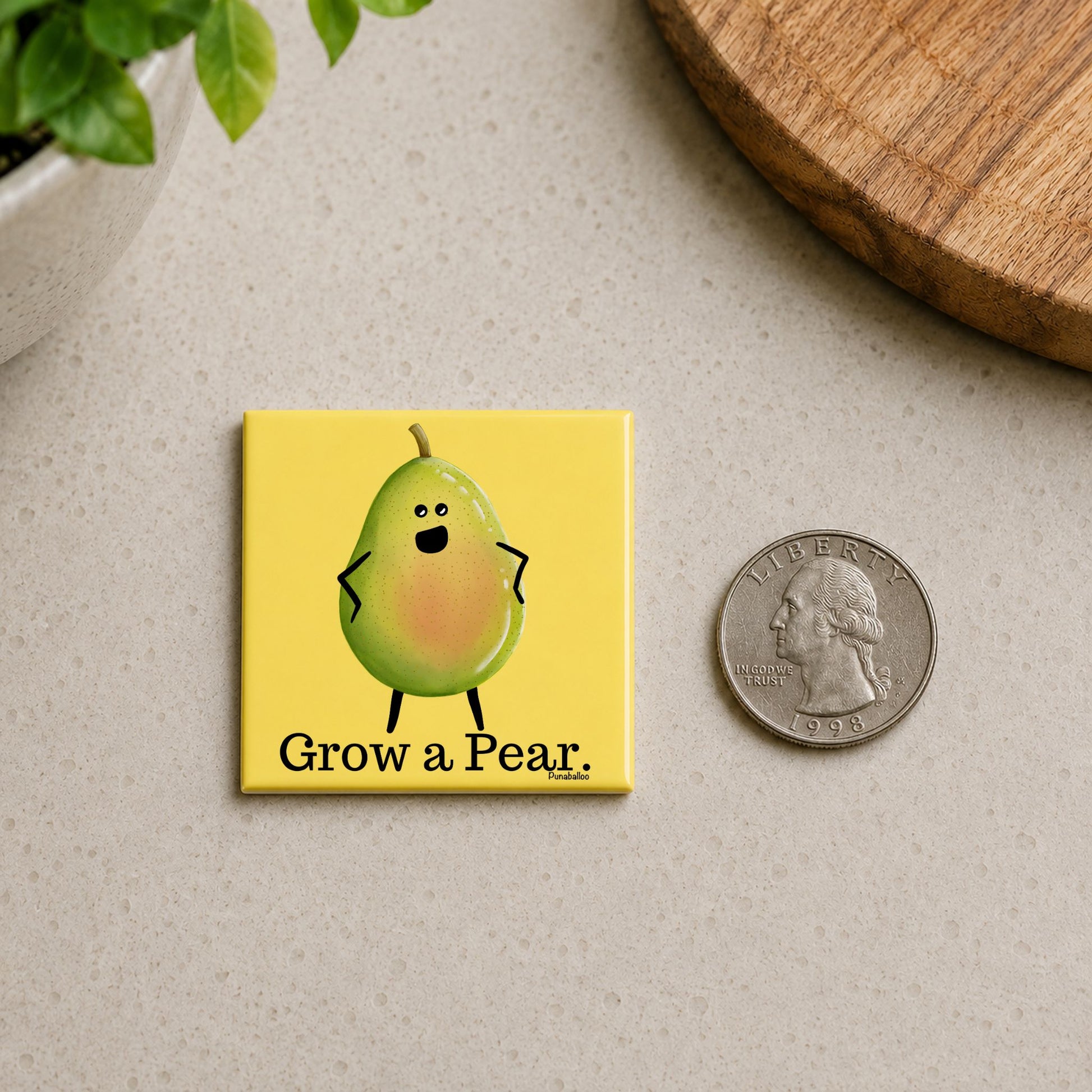 Grow a Pear pear pun magnet on a countertop beside a quarter for size