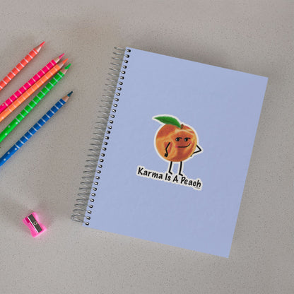Karma Is a Peach peach sticker on a notebook beside colored pencils