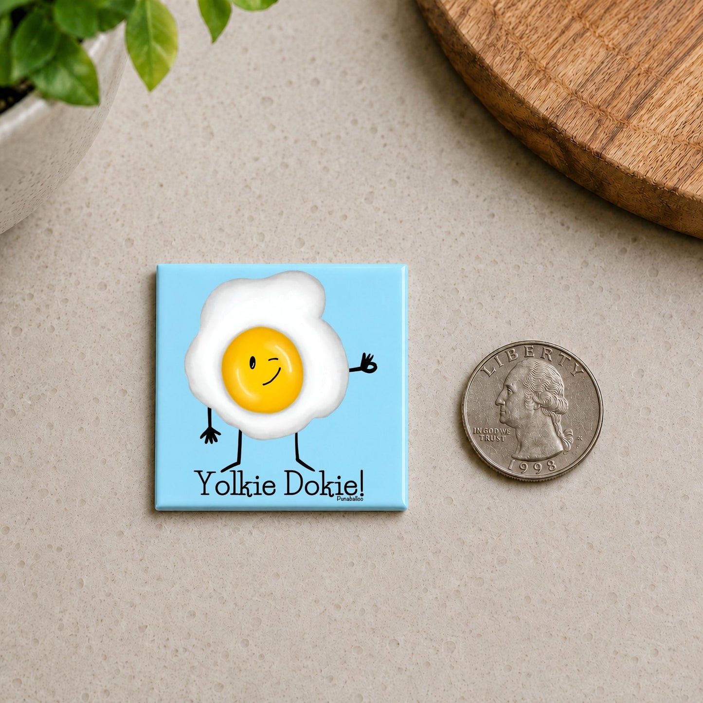 Yolkie Dokie egg pun magnet on a countertop beside a quarter for size