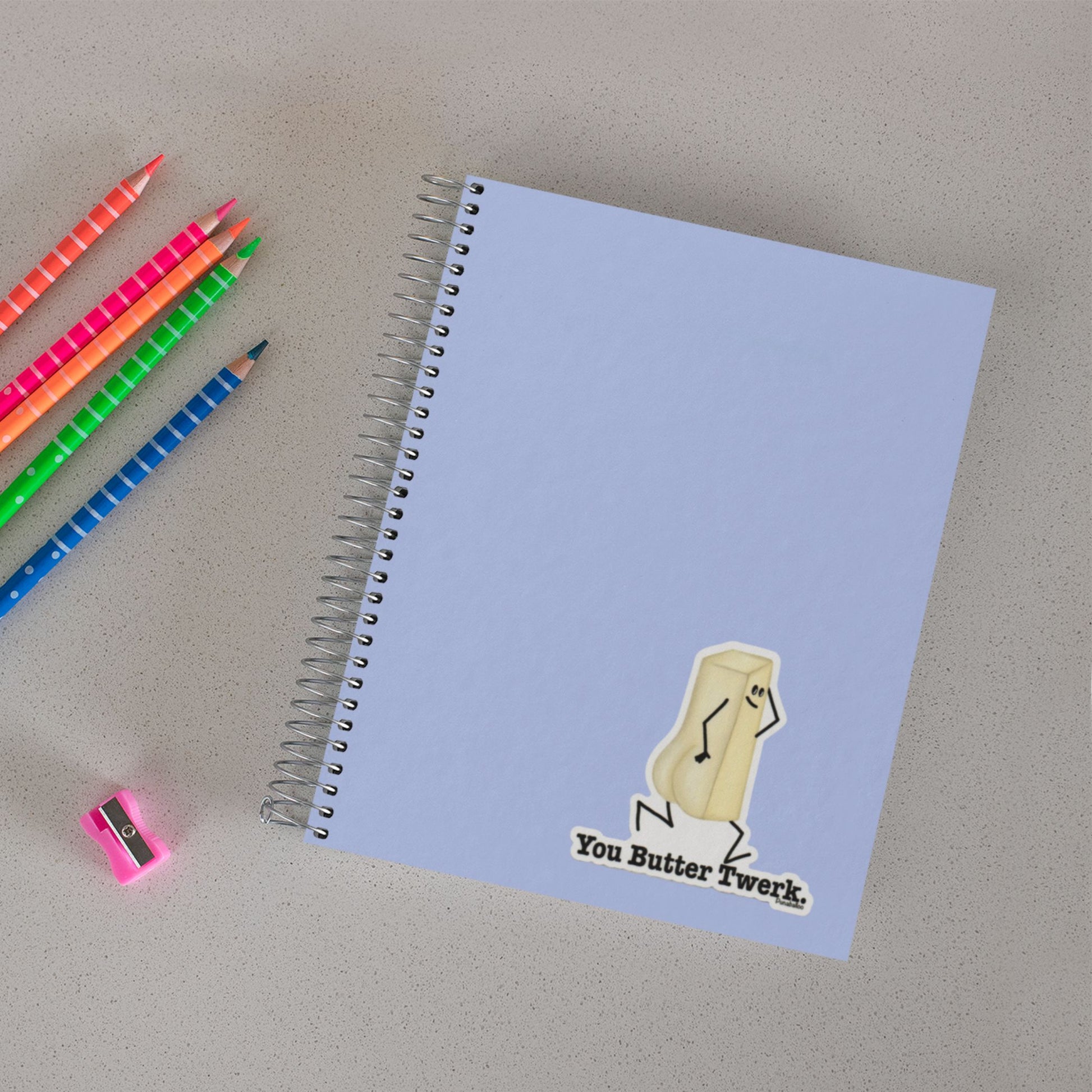 You Butter Twerk food pun sticker on a notebook beside colored pencils