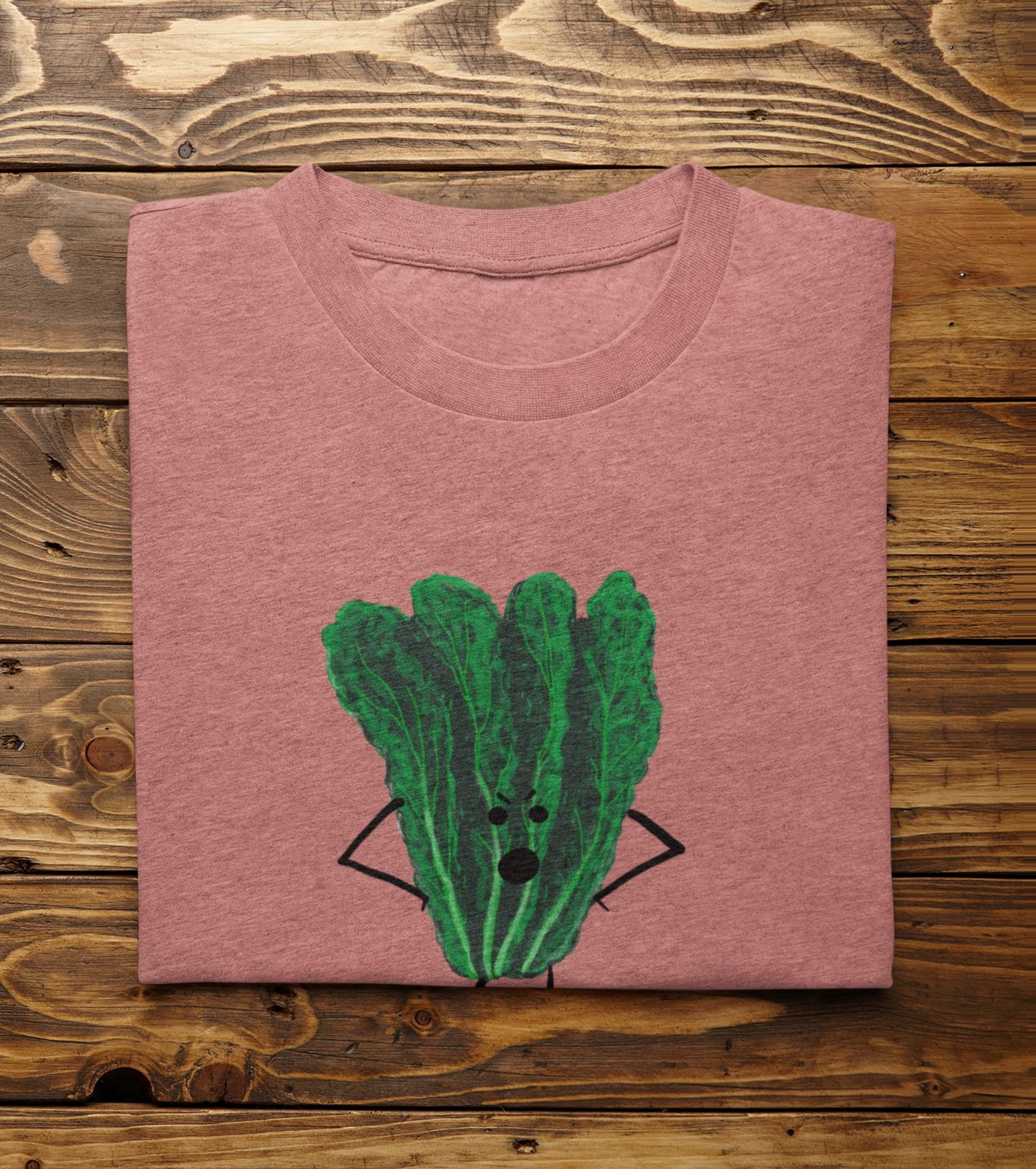 A folded light heather mauve t-shirt with Oh Kale No pun printed on the front, displayed flat on a rustic wooden plank background.