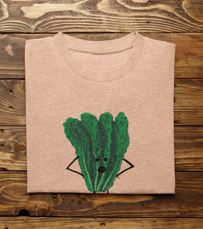 A folded light heather peach t-shirt with Oh Kale No pun printed on the front, displayed flat on a rustic wooden plank background.