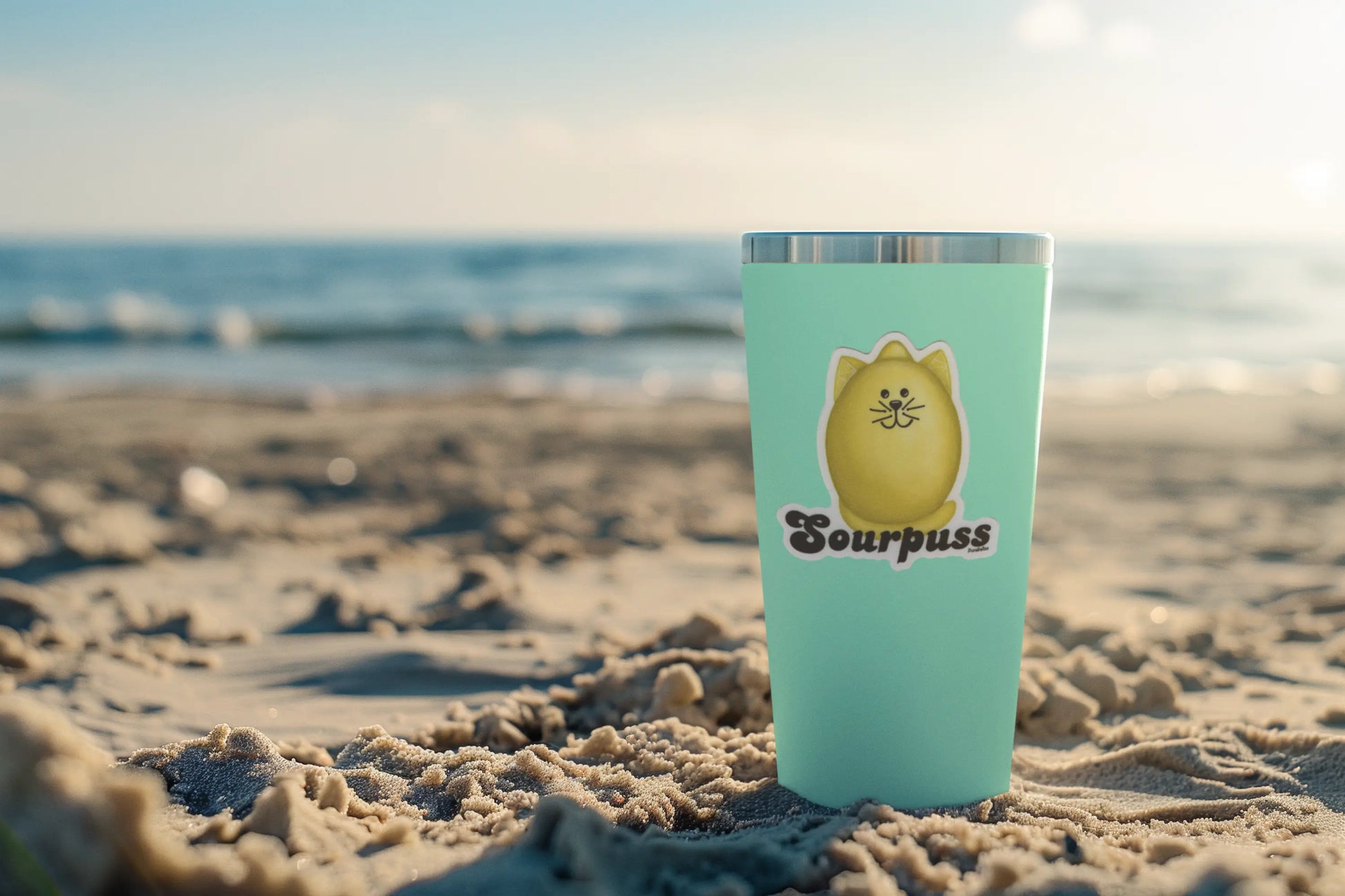 Fruit Pun Sticker with lemon graphic and sourpuss caption on a turquoise tumbler on the beach.