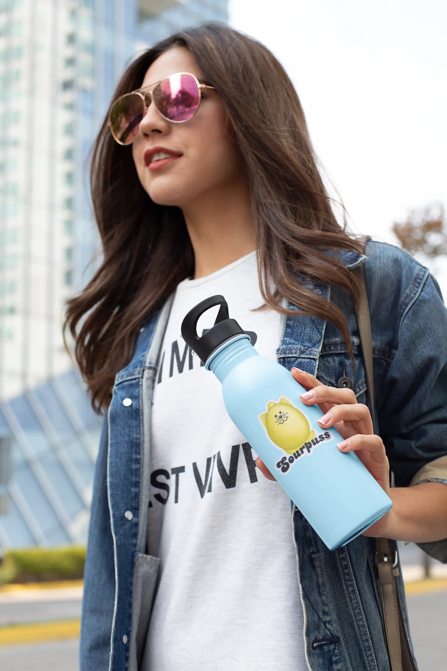 Woman holding a water bottle with Sourpuss lemon pun sticker on a city street