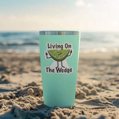 Turquoise tumbler with 'Living On The Wedge' fruit pun sticker on a sandy beach