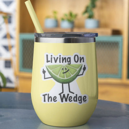Yellow wine tumbler with a sticker on it featuring a lime character and text 'Living On The Wedge' on a blurred background.