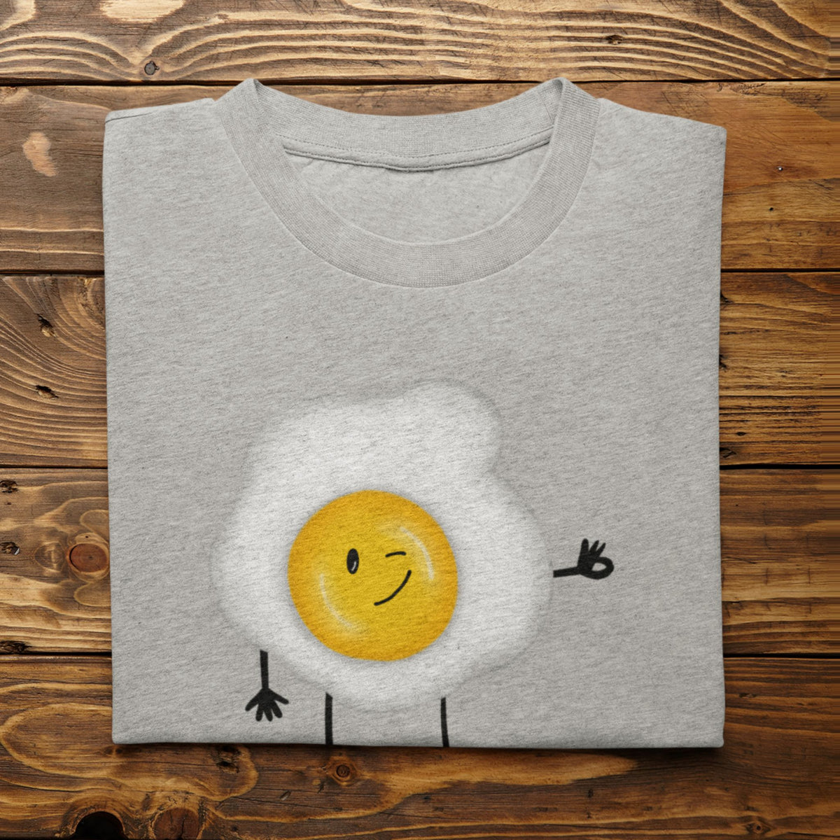 Athletic Heather Yolkie Dokie fried egg pun T-shirt folded on a rustic wood background