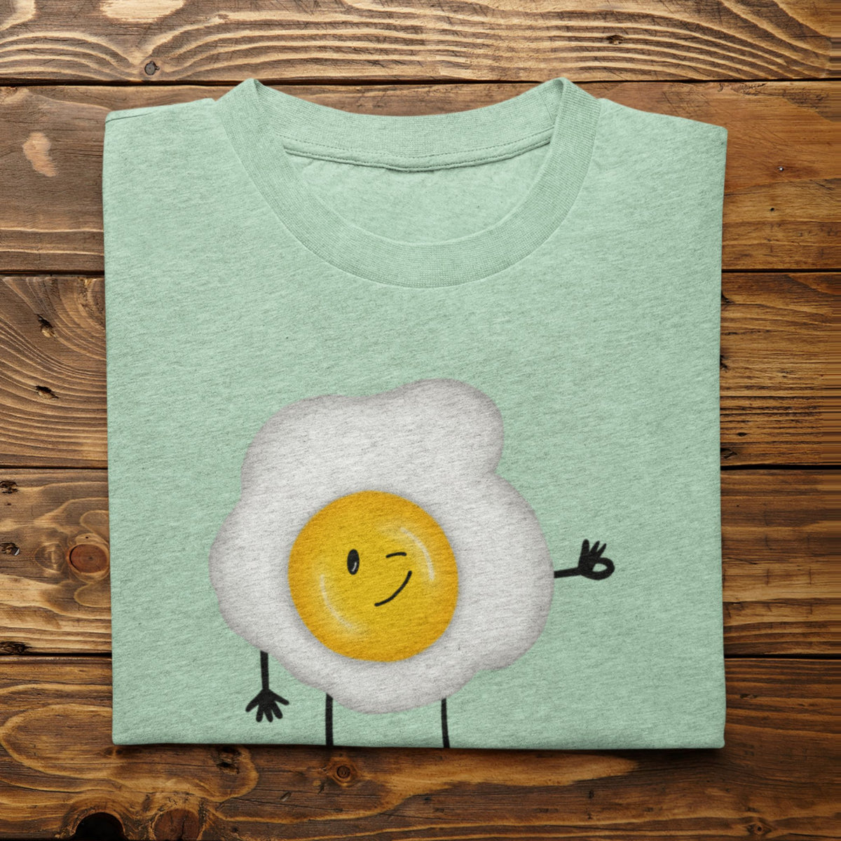 Heather Mint Yolkie Dokie fried egg pun T-shirt folded on a rustic wood background