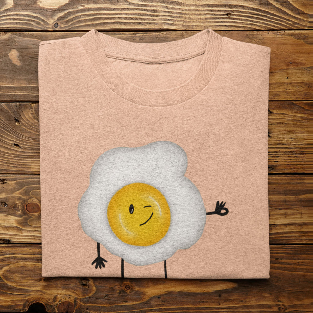 Heather Peach Yolkie Dokie fried egg pun T-shirt folded on a rustic wood background