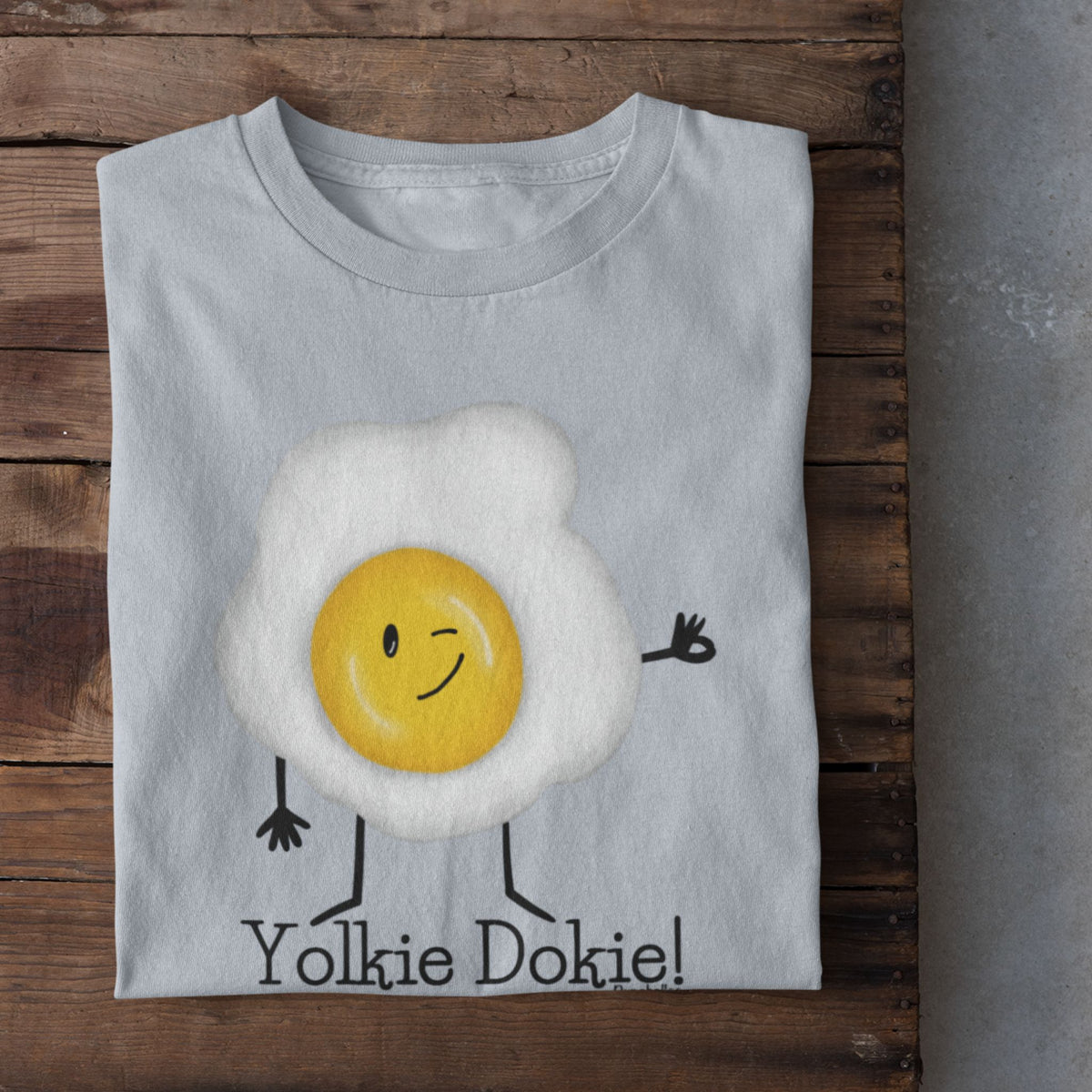 Light Blue Yolkie Dokie fried egg pun T-shirt folded on a rustic wood background