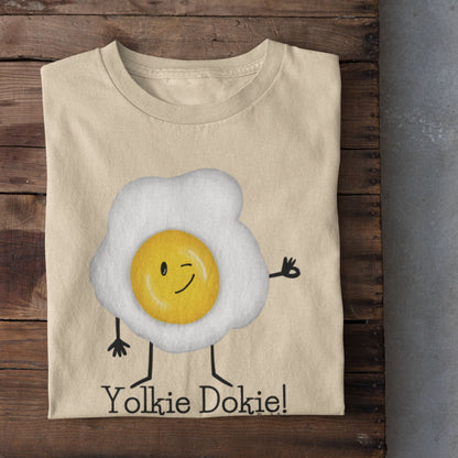 Soft Cream Yolkie Dokie fried egg pun T-shirt folded on a rustic wood background