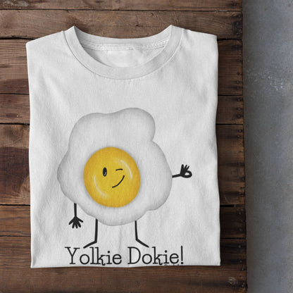 White Yolkie Dokie fried egg pun T-shirt folded on a rustic wood background